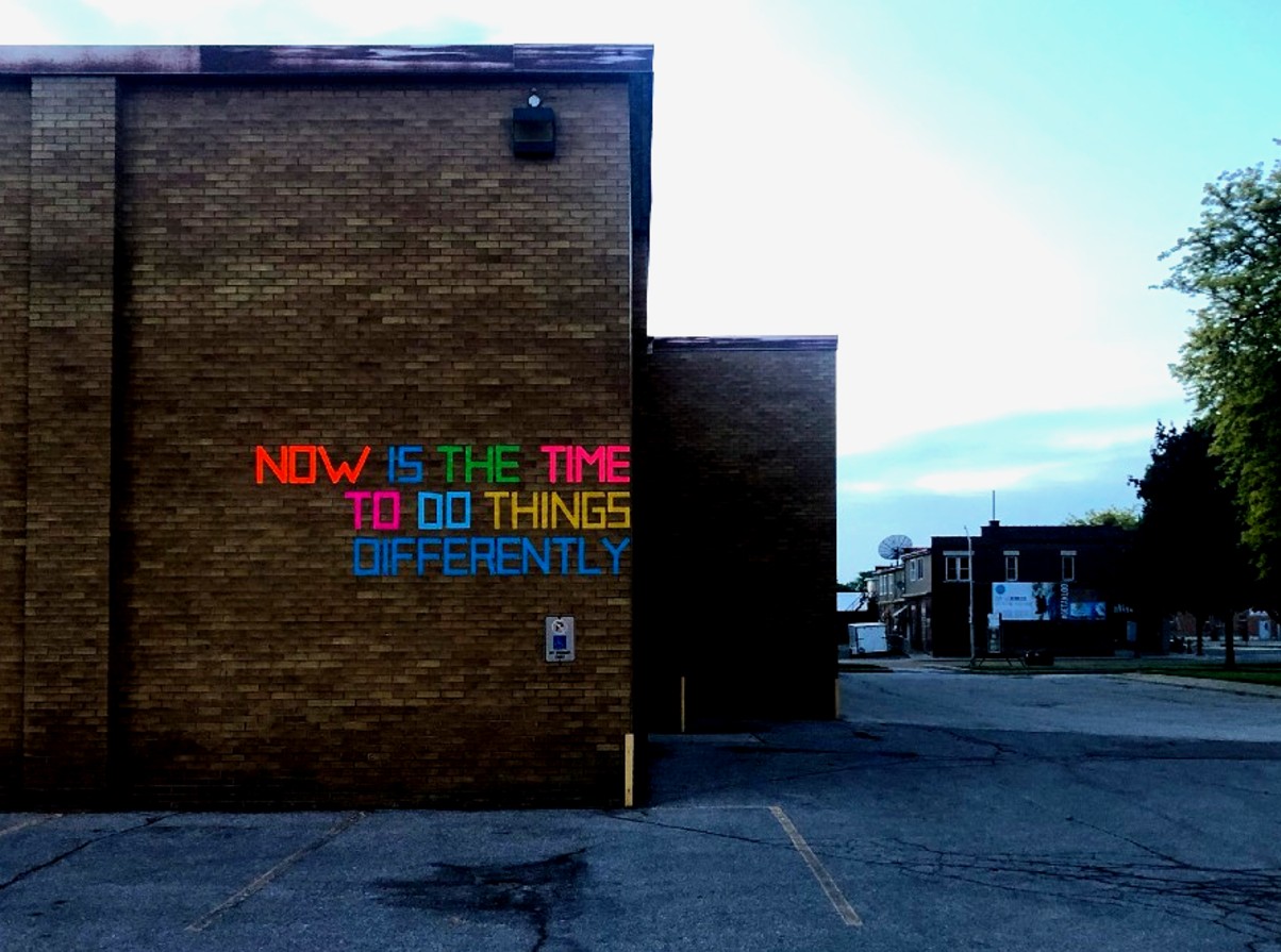 A brick building with NOW IS THE TIME DO DO THINGS DIFFERENTLY written on the side in colourful duct tape