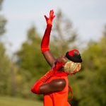 A black woman in a red dress and long red gloves reaches upwards