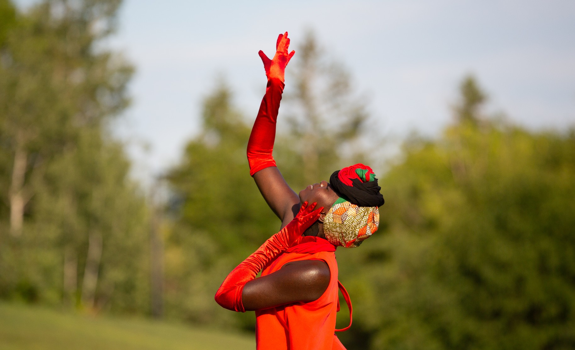 A black woman in a red dress and long red gloves reaches upwards