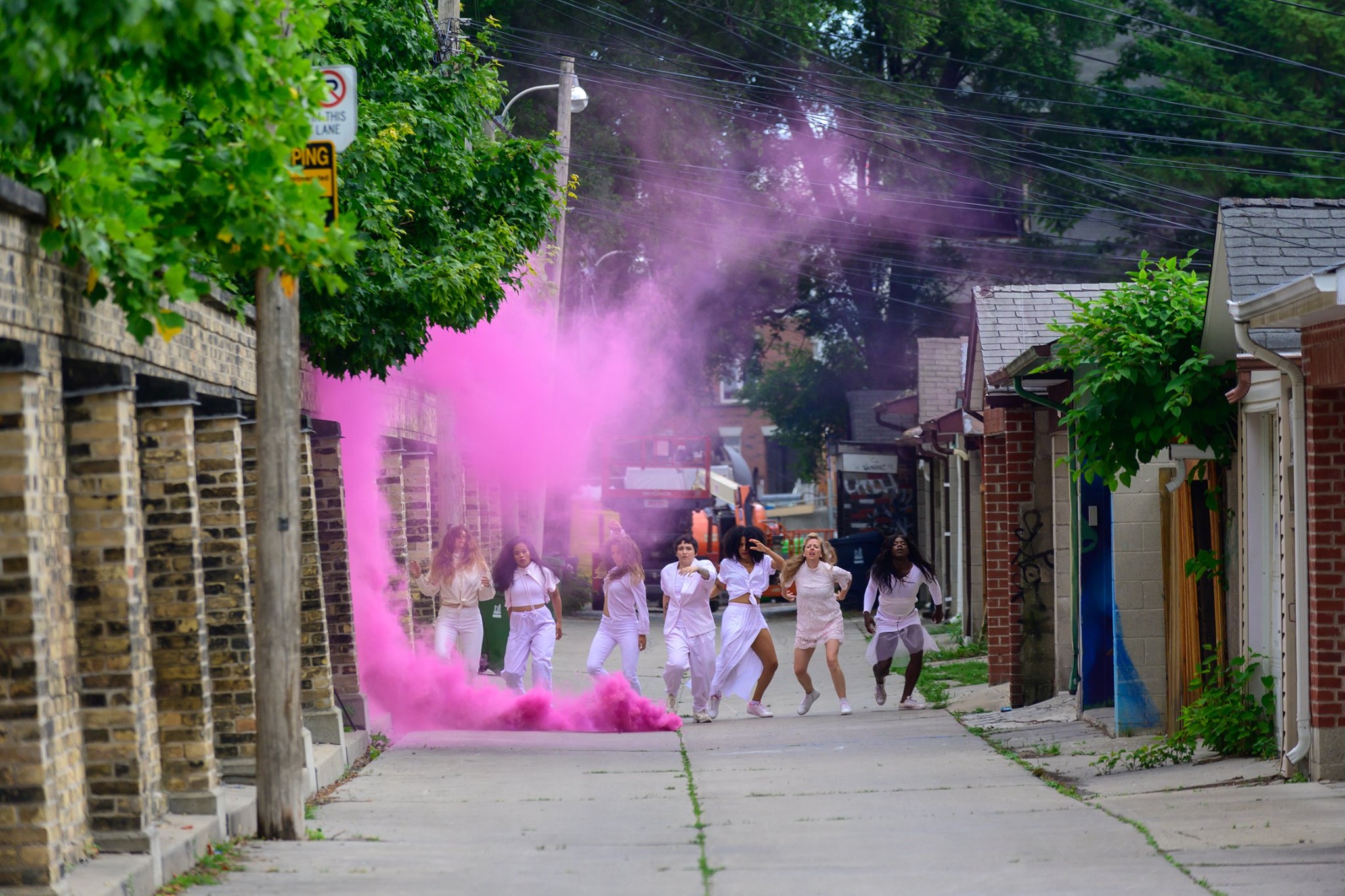 a group of people dance in an alleyway, with pink smoke billowing around them