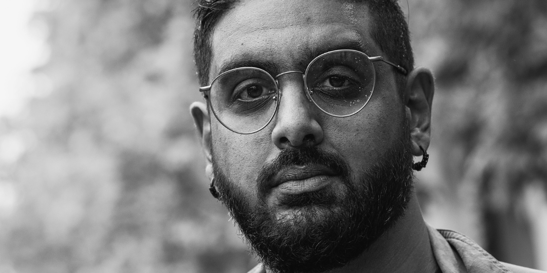 A black and white image of Jivesh with round glasses, a beard, hooped earrings and a jean jacket.