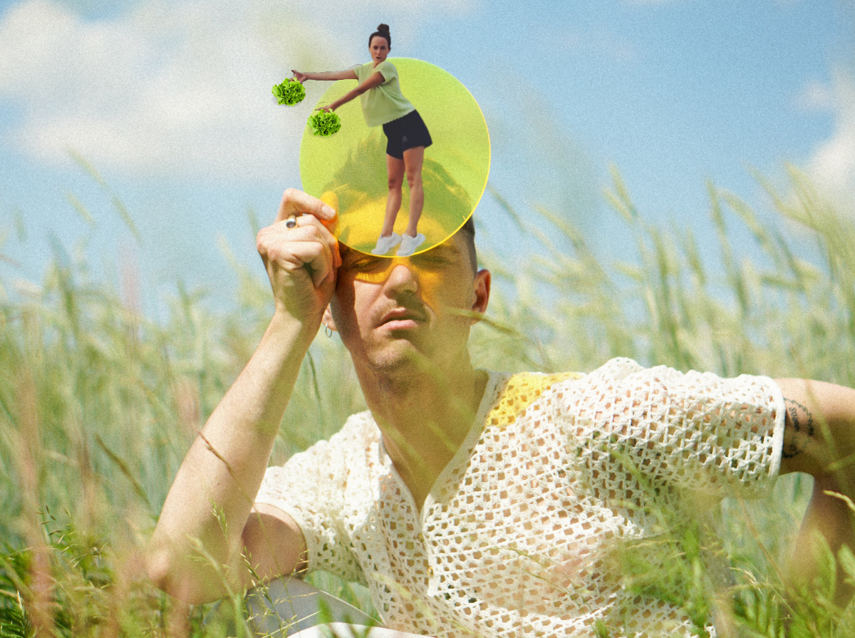 Jacob sits holding a transparent yellow disc to their forehead in a sunny field of tall green grass. Within the yellow disk, there is a small image of Alyssa cheerleading with lettuce bundles for pom poms.