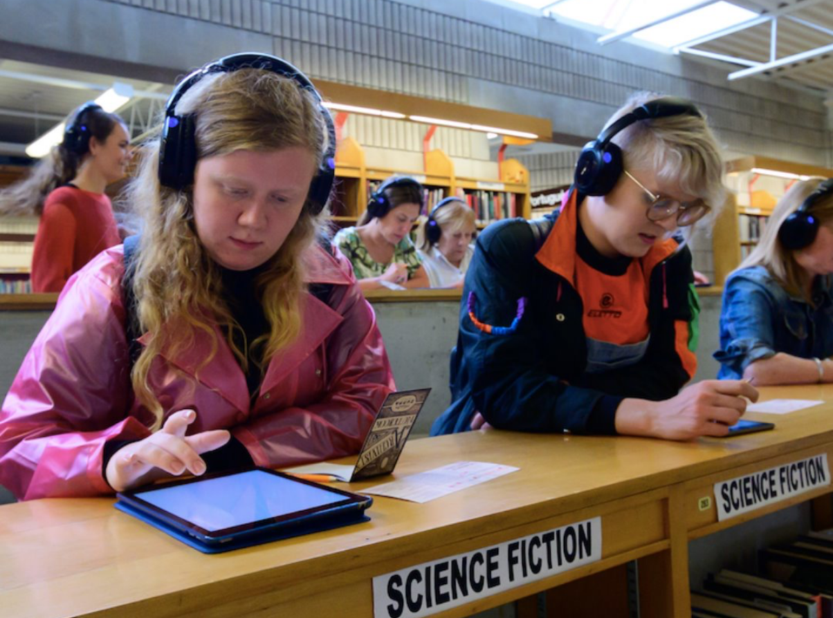 Young people in classroom using tablets with headphones.