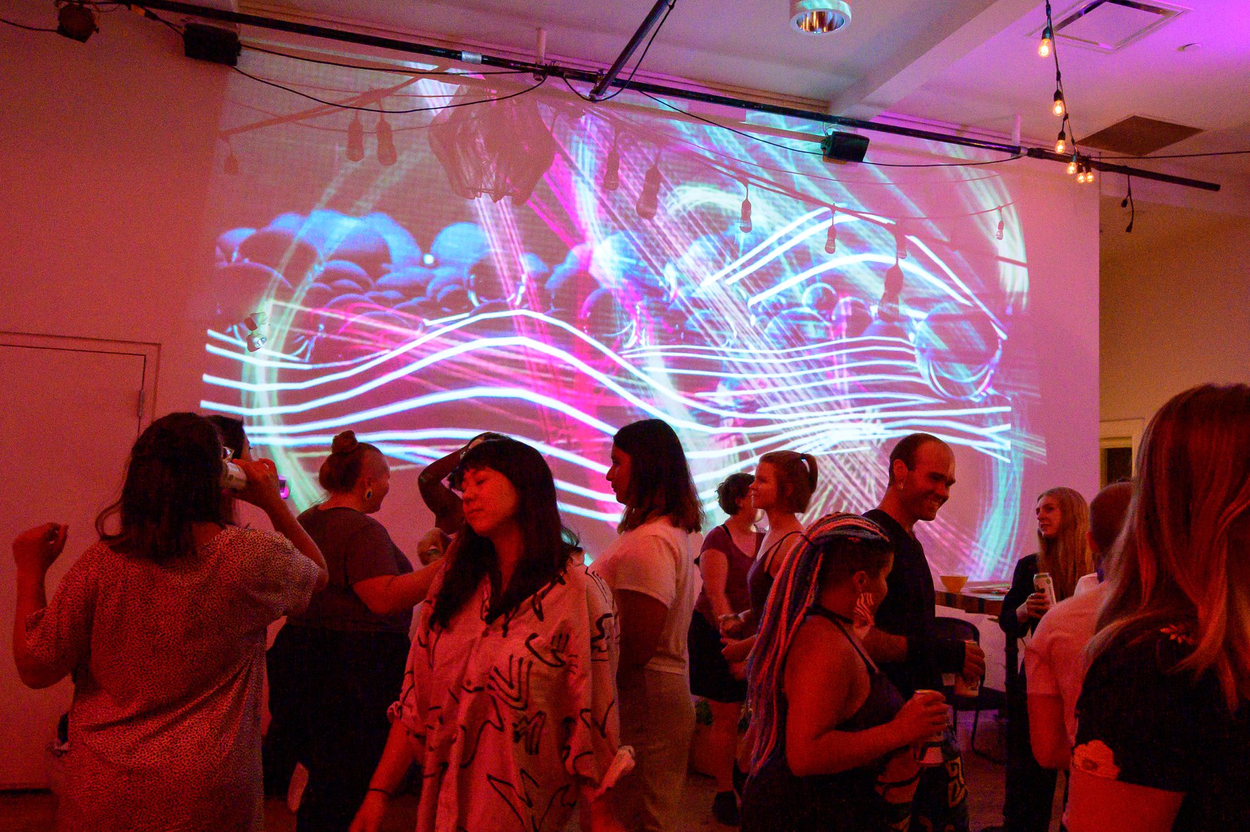 Purple and blue wavy projections on a white background, indoors, with a crowd of people dancing, talking and eating in the foreground.
